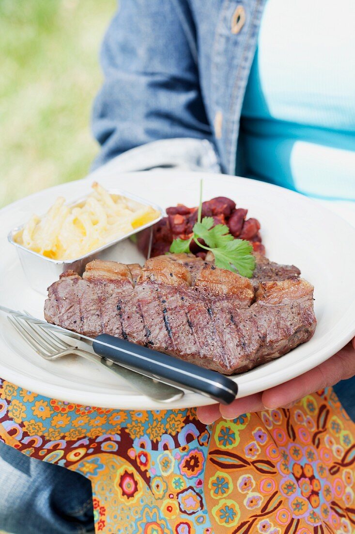 A person holding a plate of grilled beefsteak