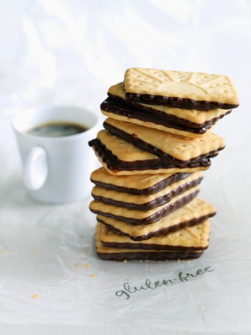 Stapel von glutenfreien Keksen mit Schokoglasur und eine Tasse Kaffee