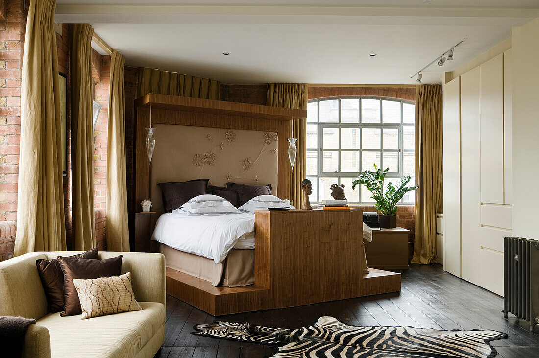 Spacious bedroom with brick wall, mullioned window and zebra carpet