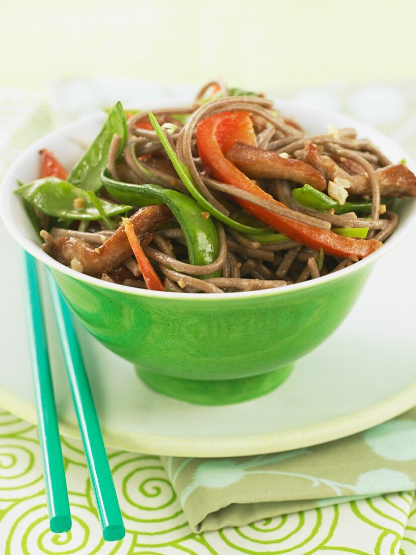 Pork and Veggie Stir Fry Over Soba Noodles in a Green Bowl with Chopsticks