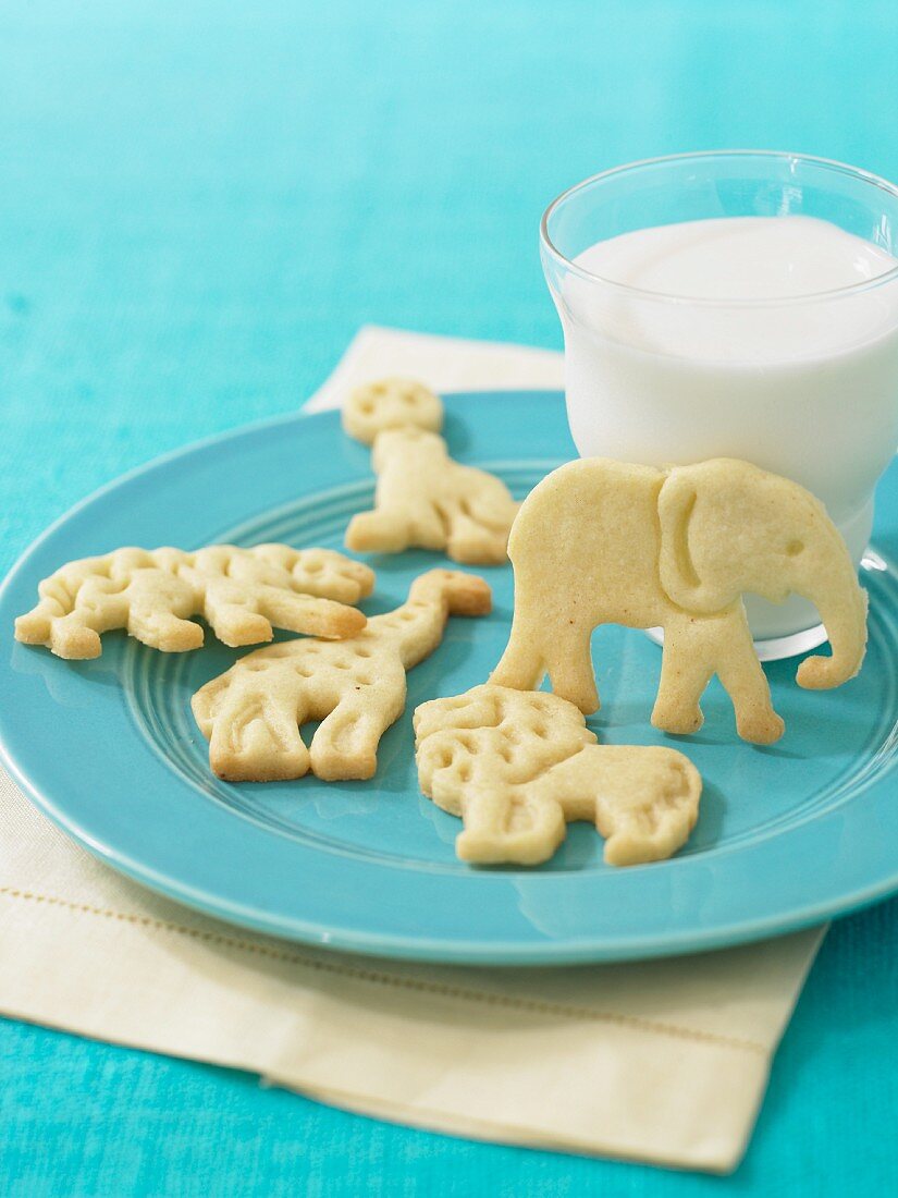 Tierförmige Kekse und ein Glas Milch auf einem blauen Teller