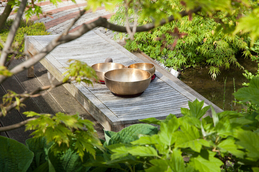 Goldene Schalen auf Holzsteg im grünen Garten mit Teich