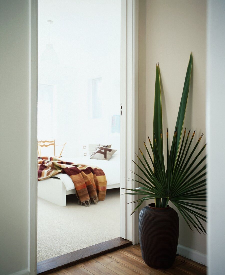 Bodenvase mit Palmenblättern neben offener Tür und Blick auf das Bett