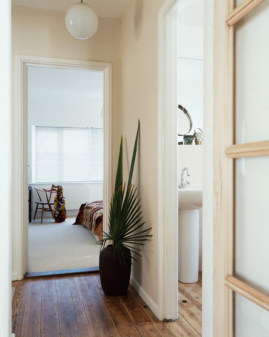 Floor vase with palm leaves next to open door showing view of bedroom