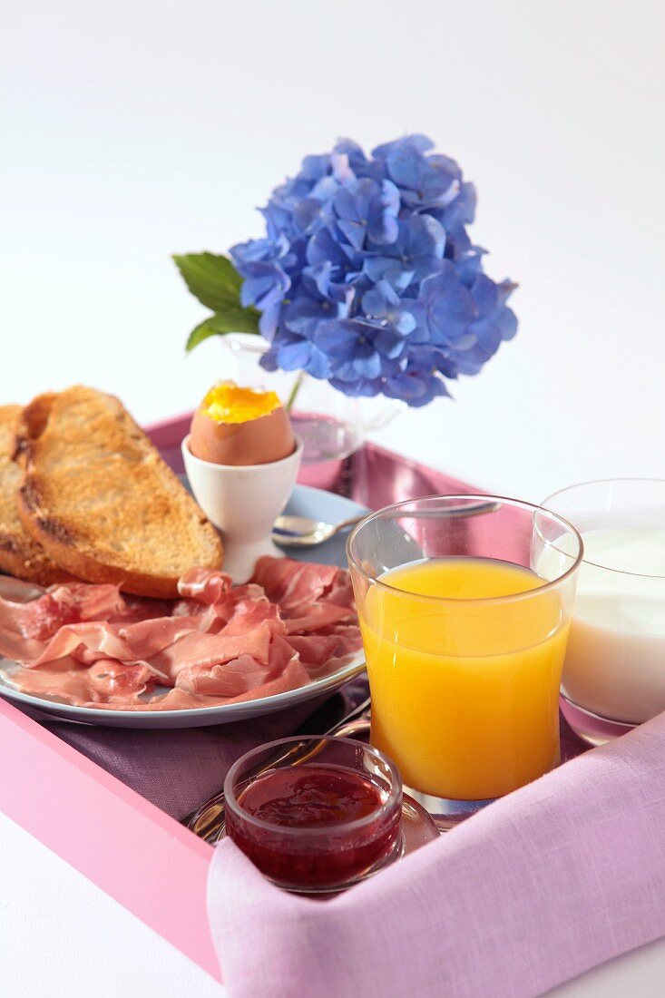 A breakfast tray with egg, toast, ham and orange juice
