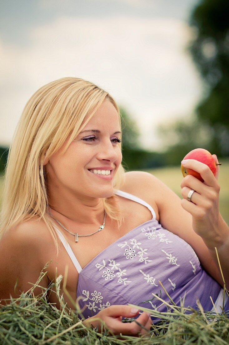 Blonde Frau liegt im Heu und hält einen Apfel