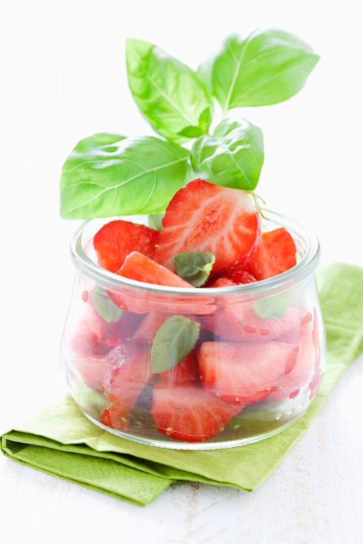 Strawberry salad with basil in glass pot on green napkin