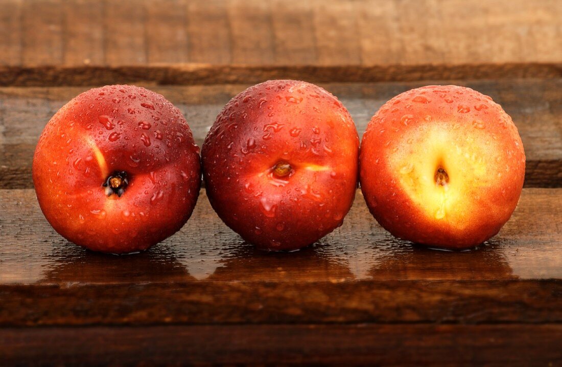 Three nectarines with droplets of water on wooden crate