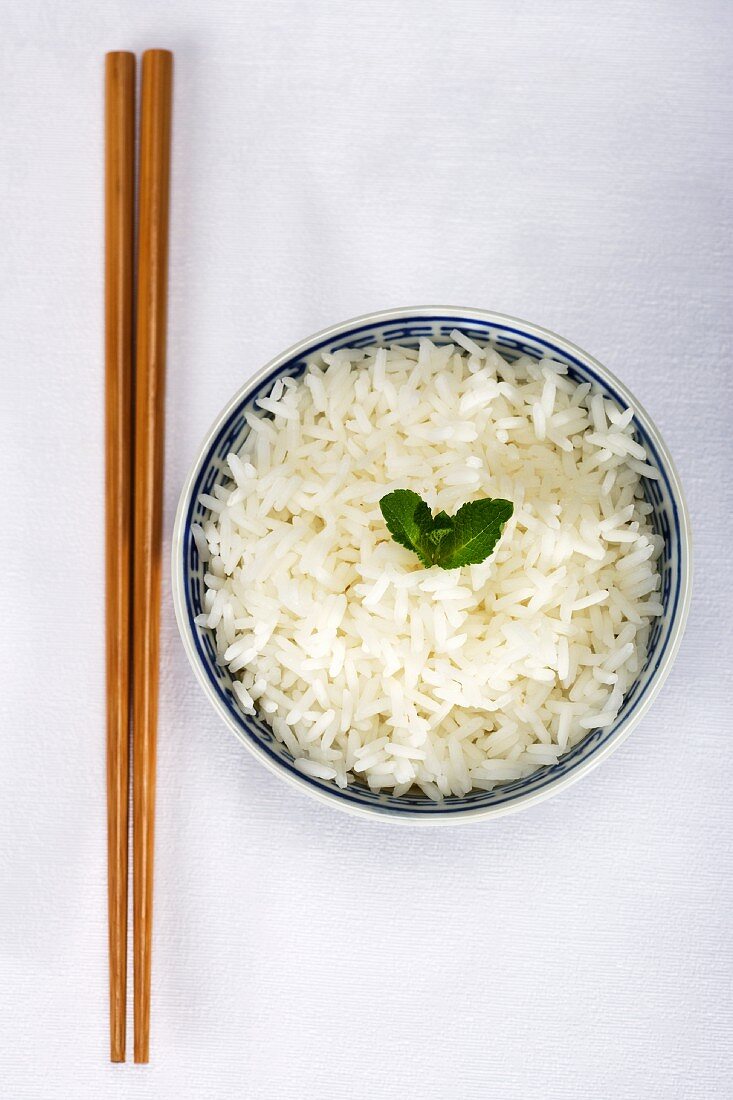 Chopsticks and a bowl of rice garnished with a mint leaf
