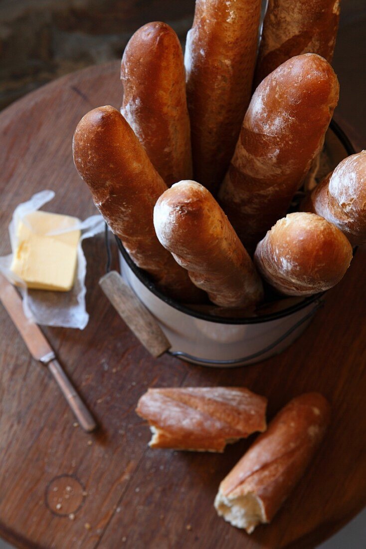 Baguettes in bucket and butter on wooden board (top view)