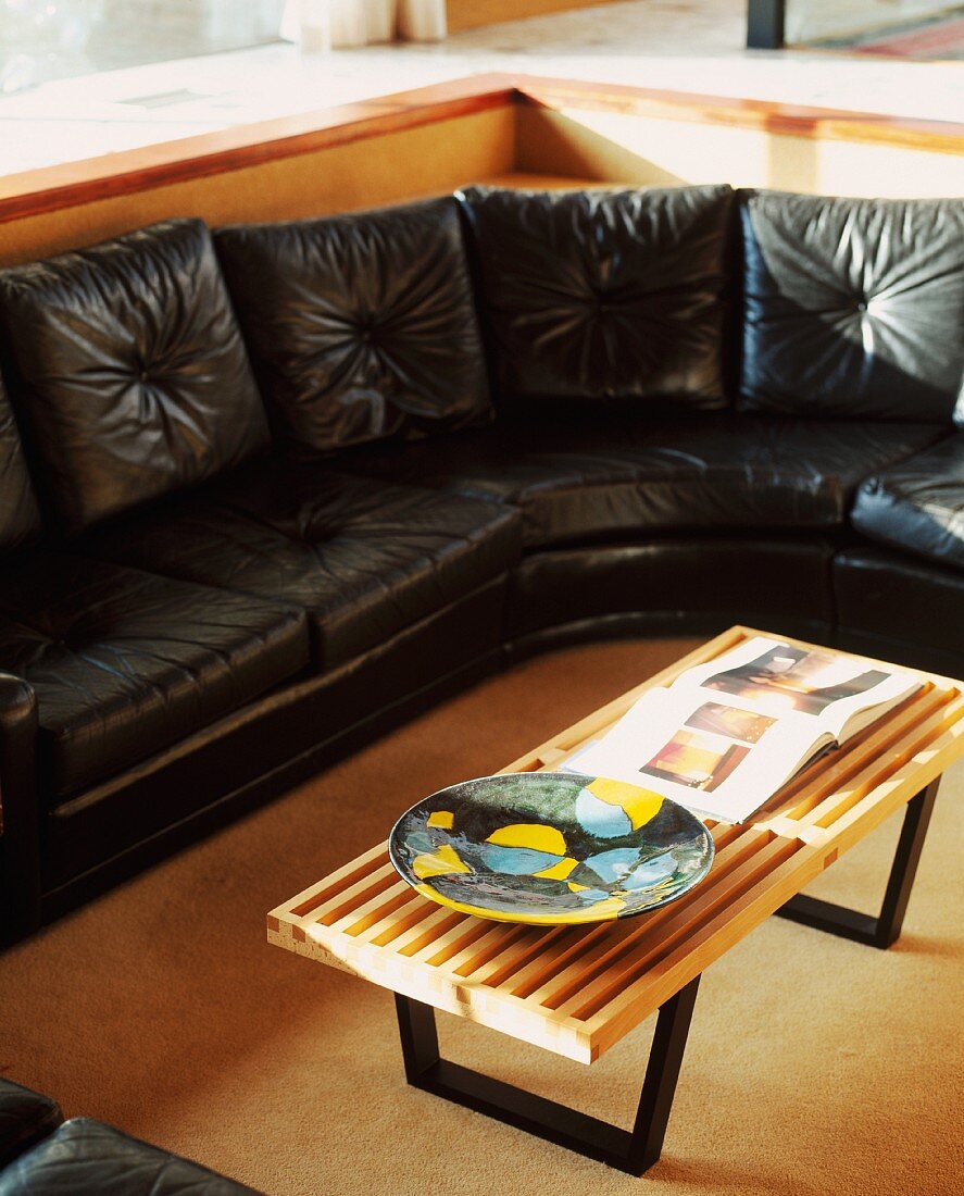 Coffee table with top made of light wooden slats in front of black leather sofa