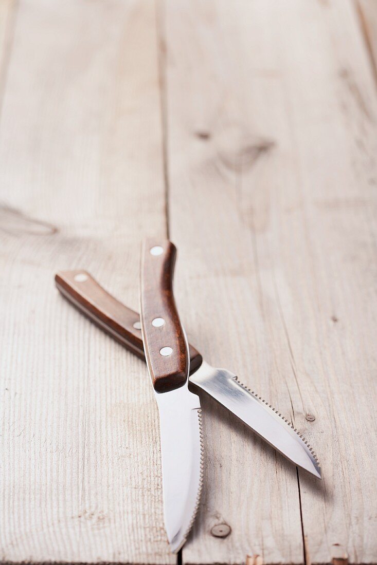 Two steak knives on a wooden surface