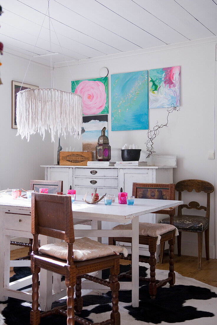 Essbereich im Landhausstil mit weißem Holztisch und farbenfrohen Wandbildern