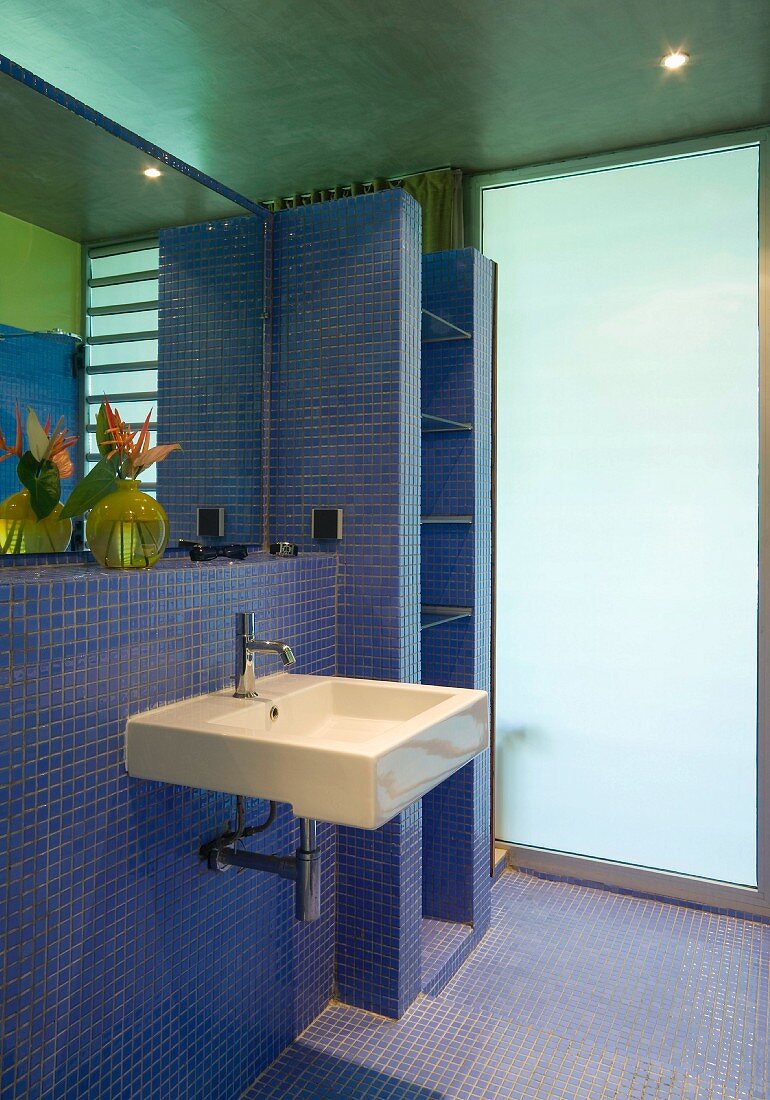 Gemauertes Regal und Designer Waschbecken in Bad mit blauen Mosaikfliesen und Wand aus satiniertem Glas