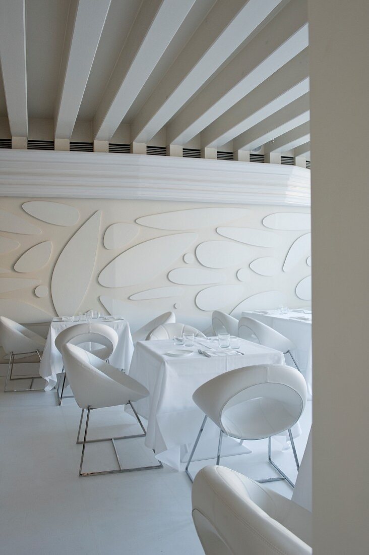 White dining room in Venetian hotel with designer chairs, modern wall relief and expressive ceiling composition
