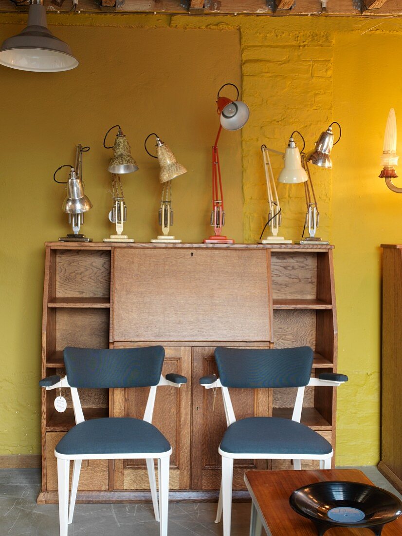 Bureau with desk lamps in front of yellow wall