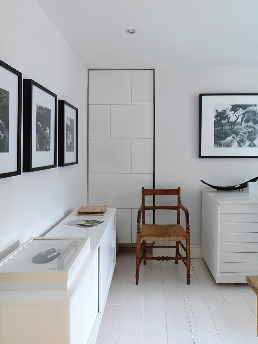 White room with sideboard, old chair and black and white photographs on the walls