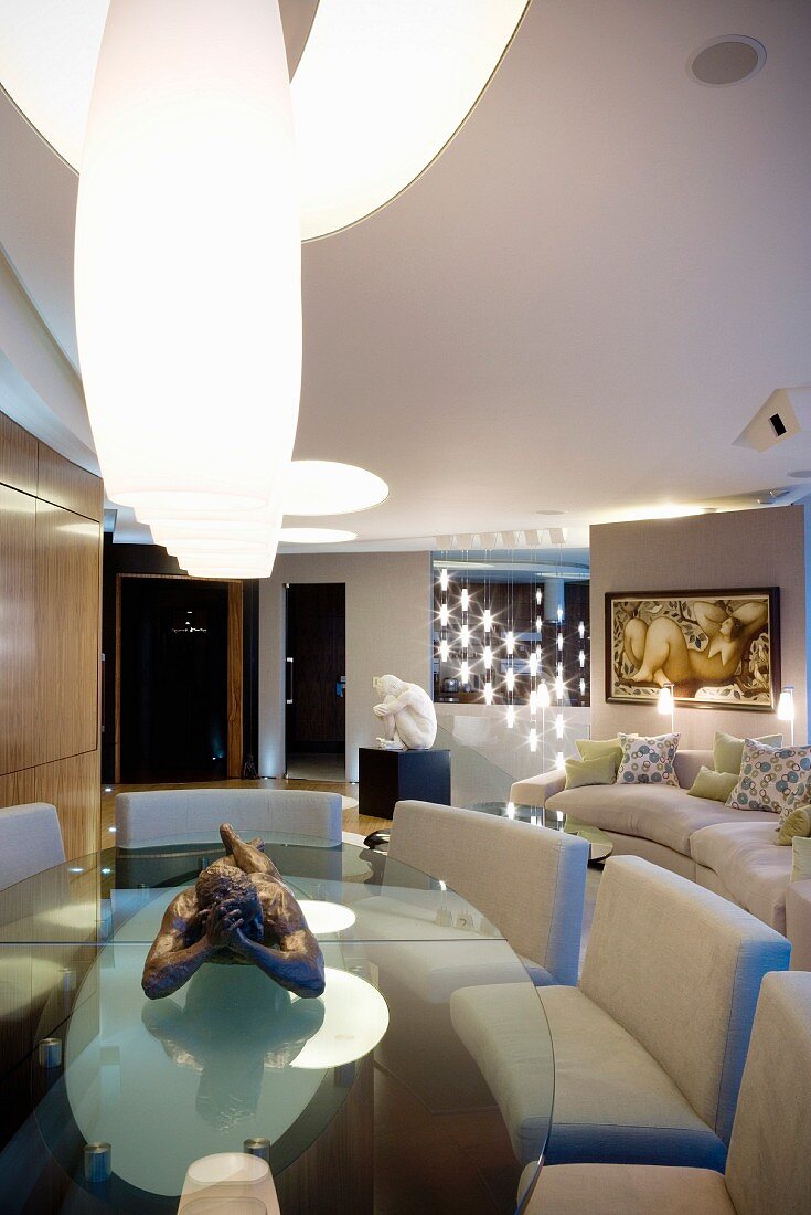 White lamps hanging over oval glass table with upholstered benches