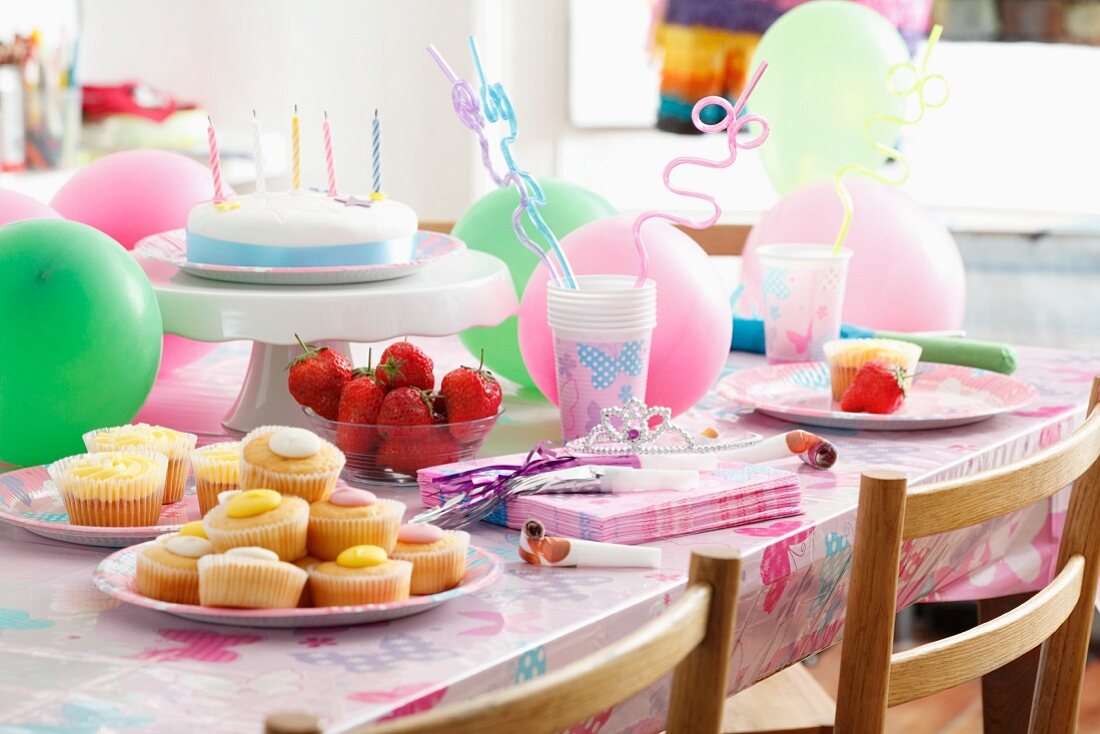 Fairy cakes, fresh strawberries and a birthday cake for children on a table with party decorations