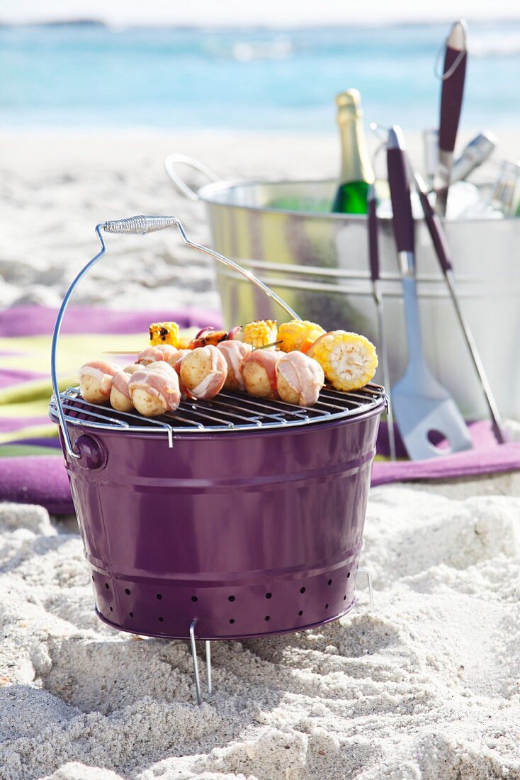 Bucket barbecue with skewers on sandy beach