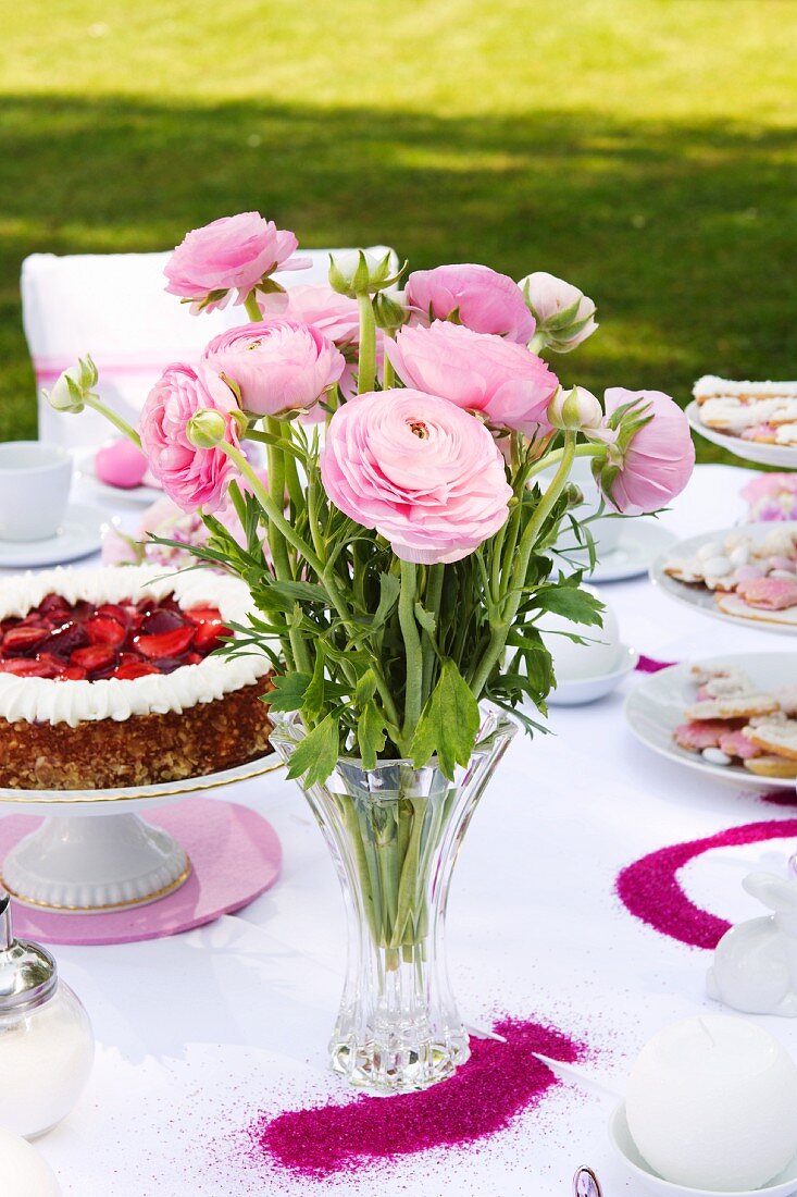 Pink ranunculus and strawberry cake on table set for afternoon tea