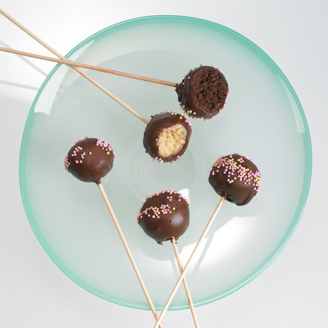 Cake pops with chocolate icing and sugar strands, one with a bite taken out