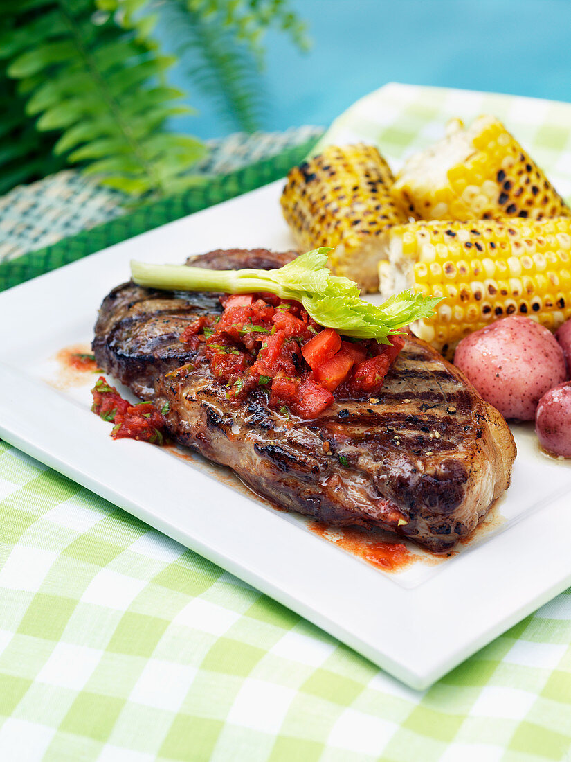 Grilled beef steak with tomato salsa and corn on the cob