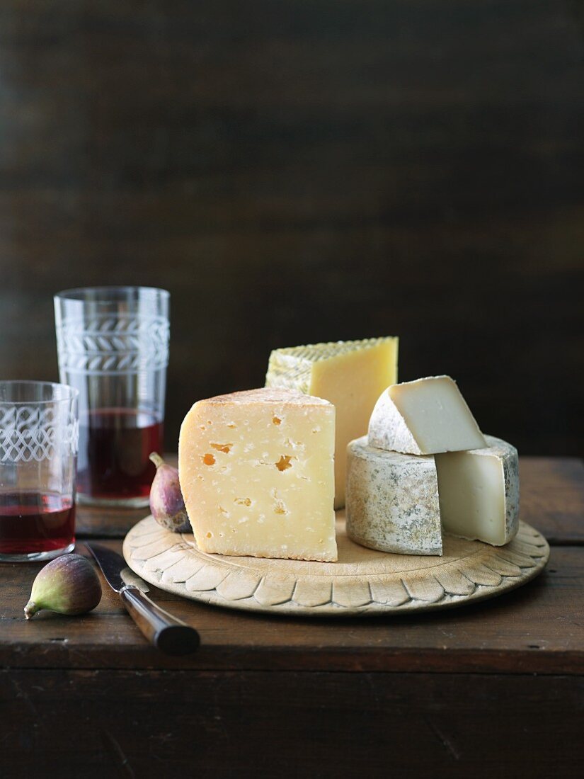 Assortment of Cheese on a Wooden Plate; Aged Goat Cheese, Gran Queso and Manchego; Figs and Red wine