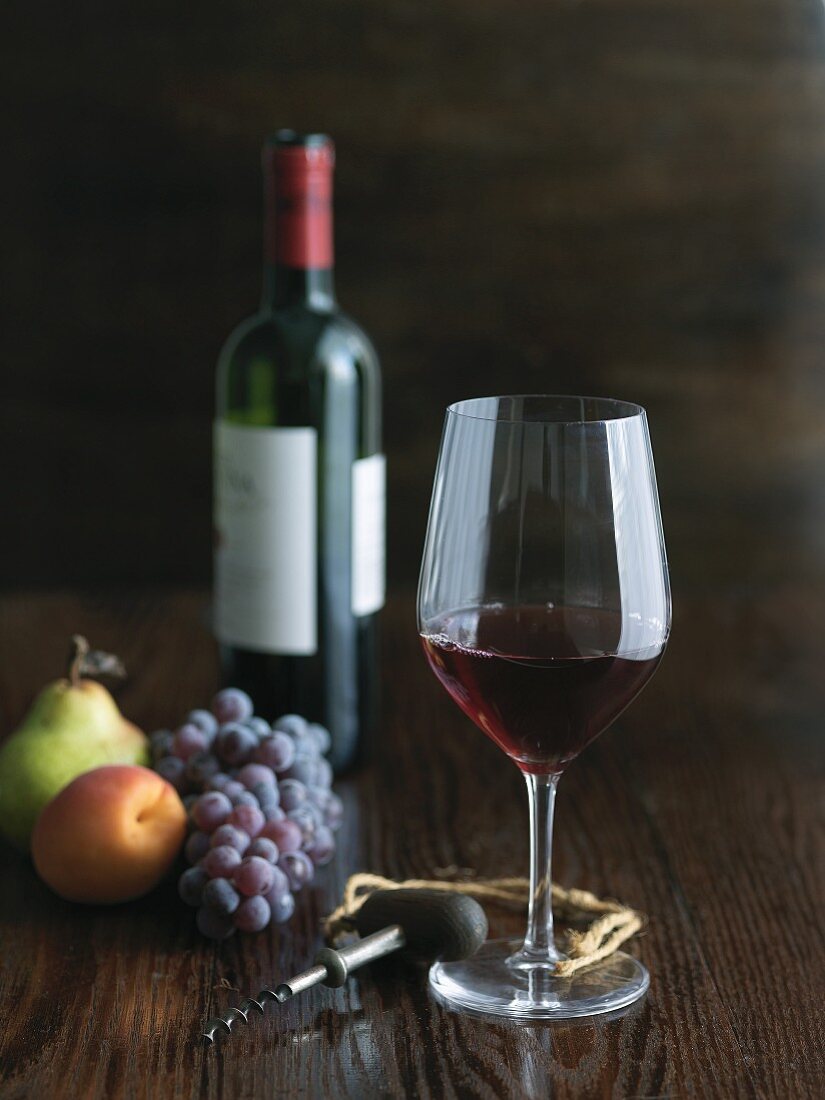Stillleben mit Rotweinglas, Korkenzieher, Obst & Weinflasche