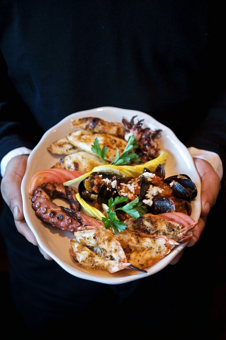 Person Holding Seafood Plate; Grilled Shrimp, Octopus and Mussels
