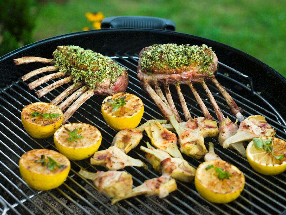 Lammkoteletts mit Kräuterkruste, Zitronenhälften und Artischocken auf dem Grill