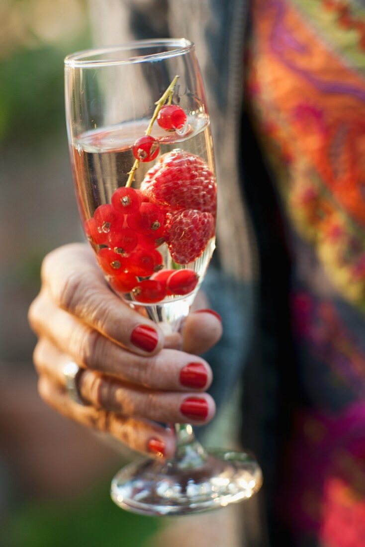 Frauenhand hält ein Glas Sekt mit Beeren