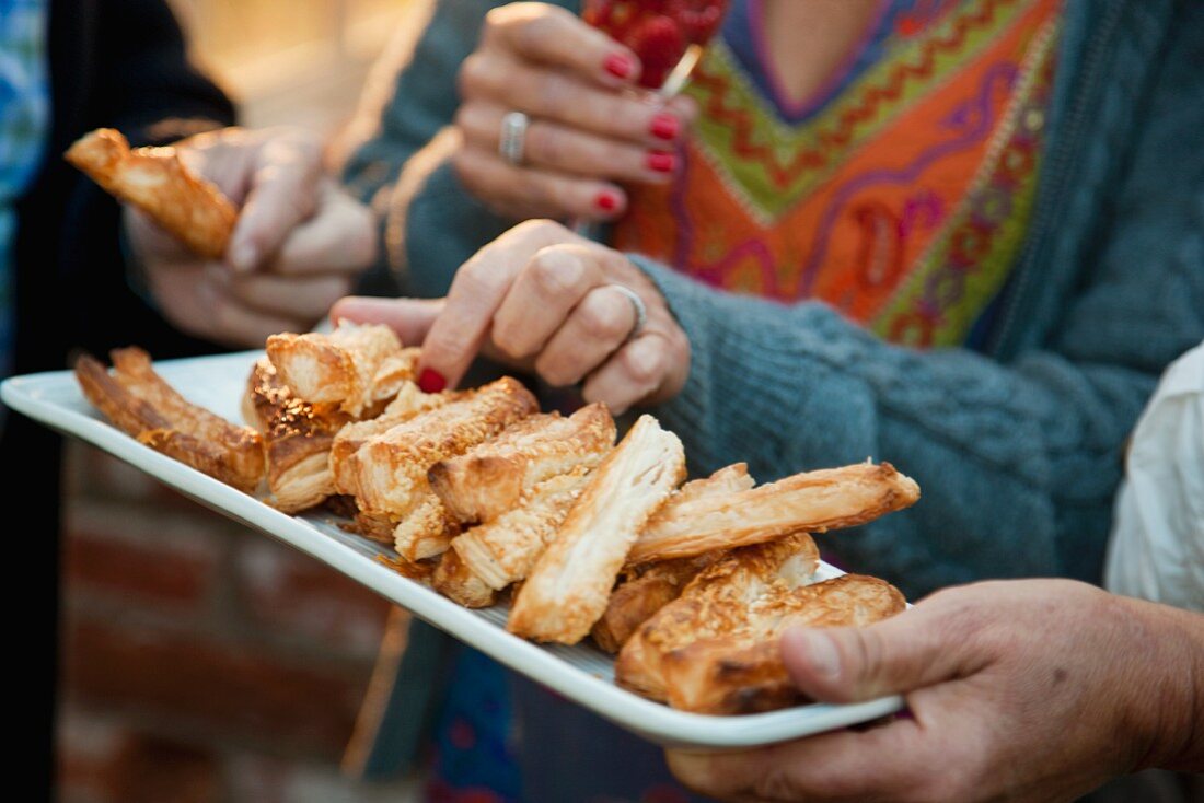 Hands taking cheese straws from tray