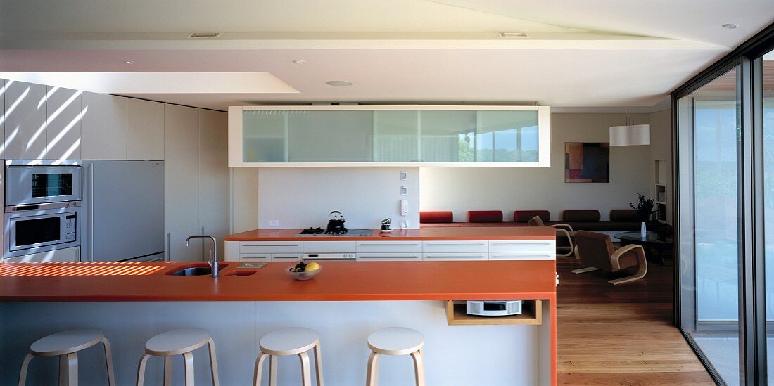 White, modern kitchen with island and orange-red work surface