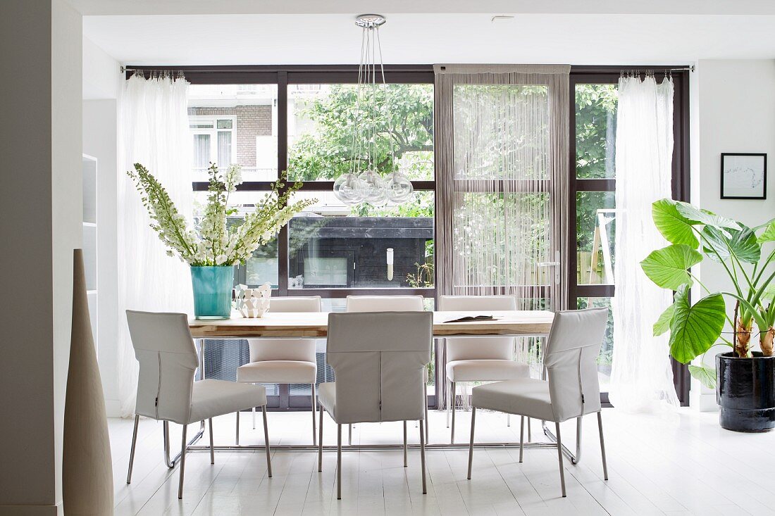 Dining area with white, upholstered chairs in front of floor-to-ceiling windows