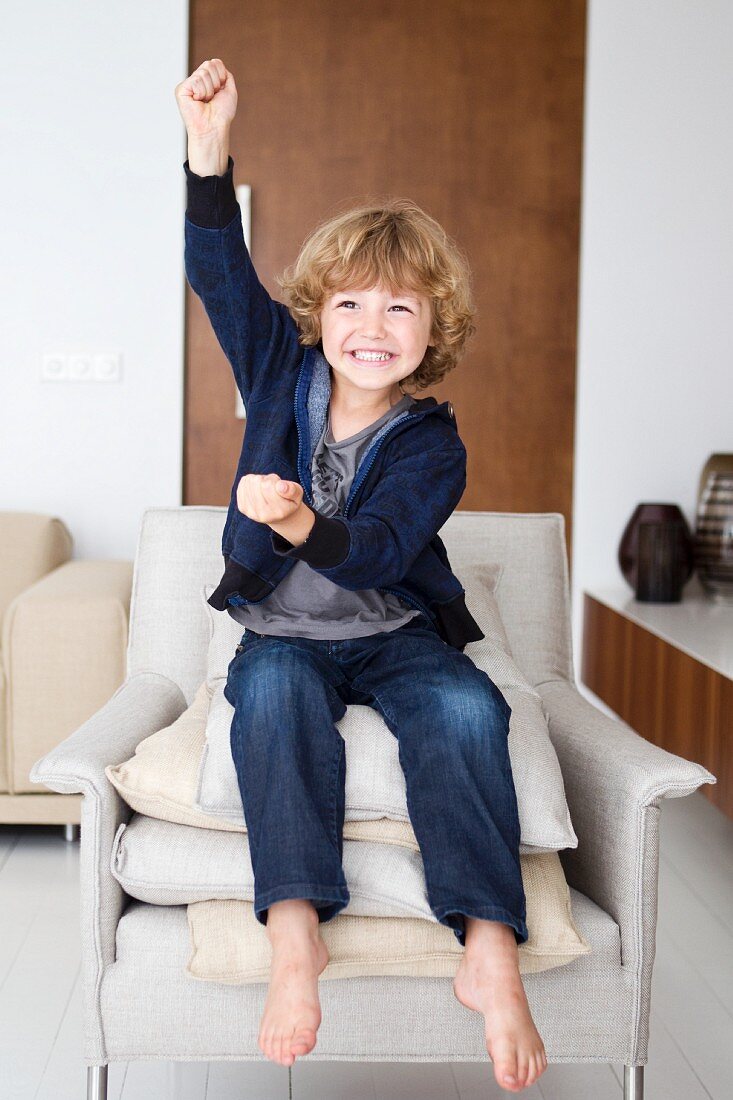 Child sitting on stack of cushions on ecru armchair