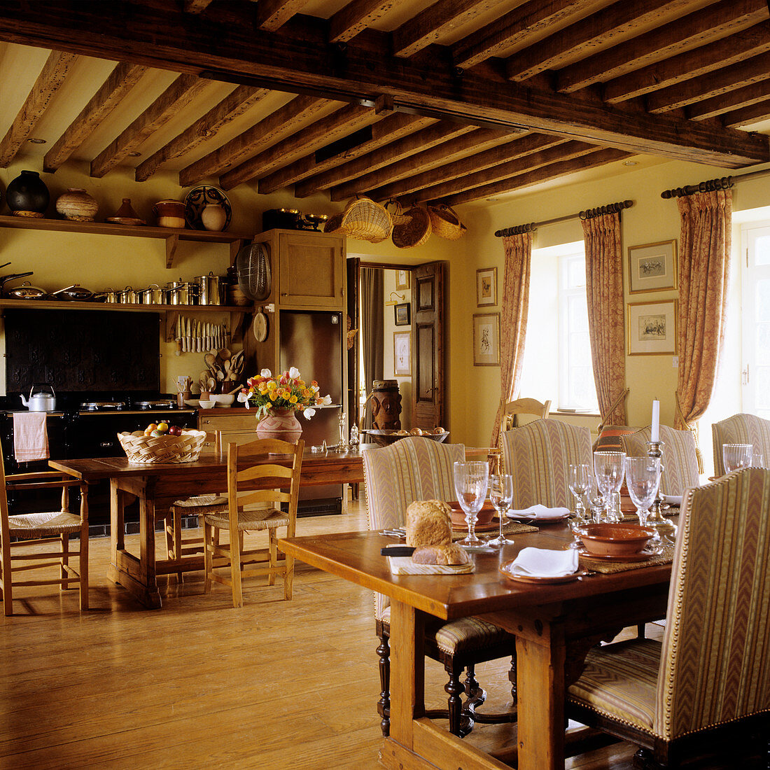 Traditionelle Esstische und offene Küche in rustikalem Gastraum mit Holzbalkendecke
