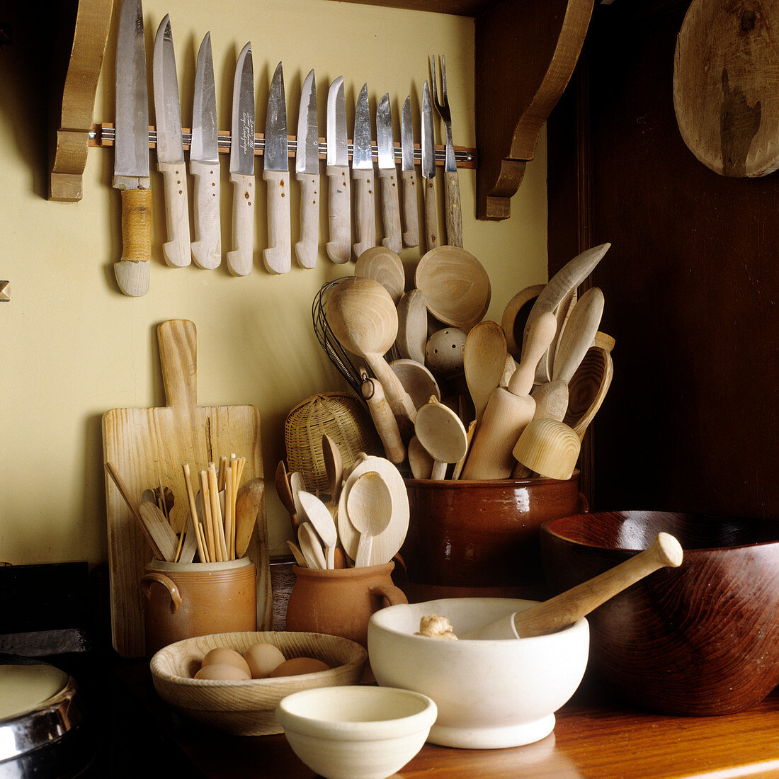 Various cooking utensils made from natural materials such as wooden spoons in ceramic pot and set of knives hanging on the wall