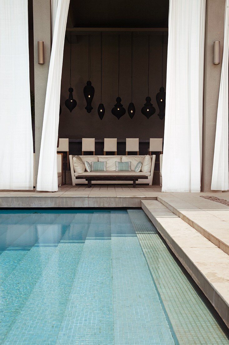 Terrace with steps leading down into pool and view of elegant sofa through open curtain