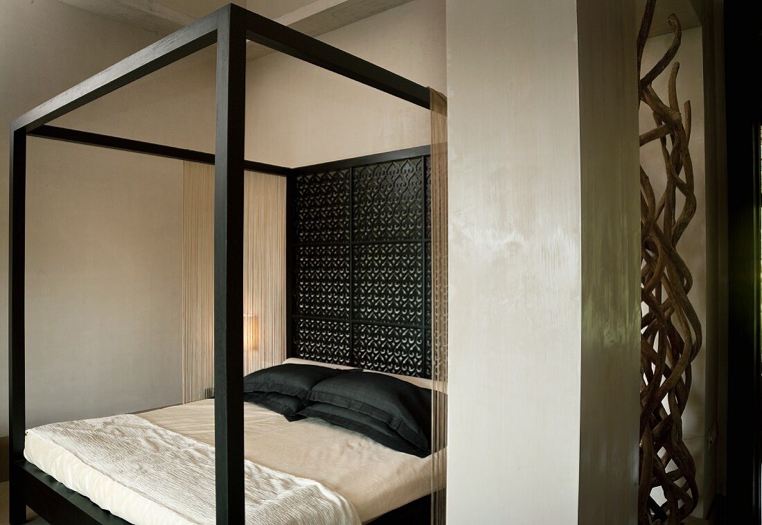 Modernes Himmelbett mit schwarzem Rahmen und Rückwand aus feinem Holzornament in elegantem Schlafraum