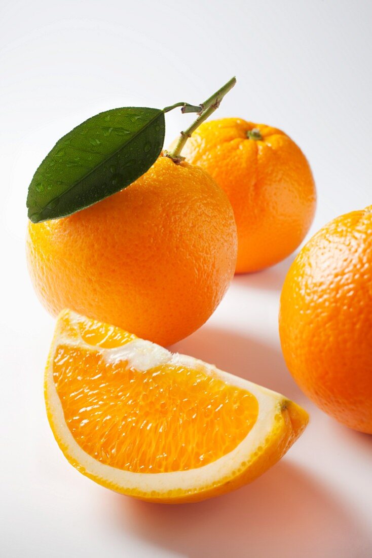 An orange wedge and whole oranges