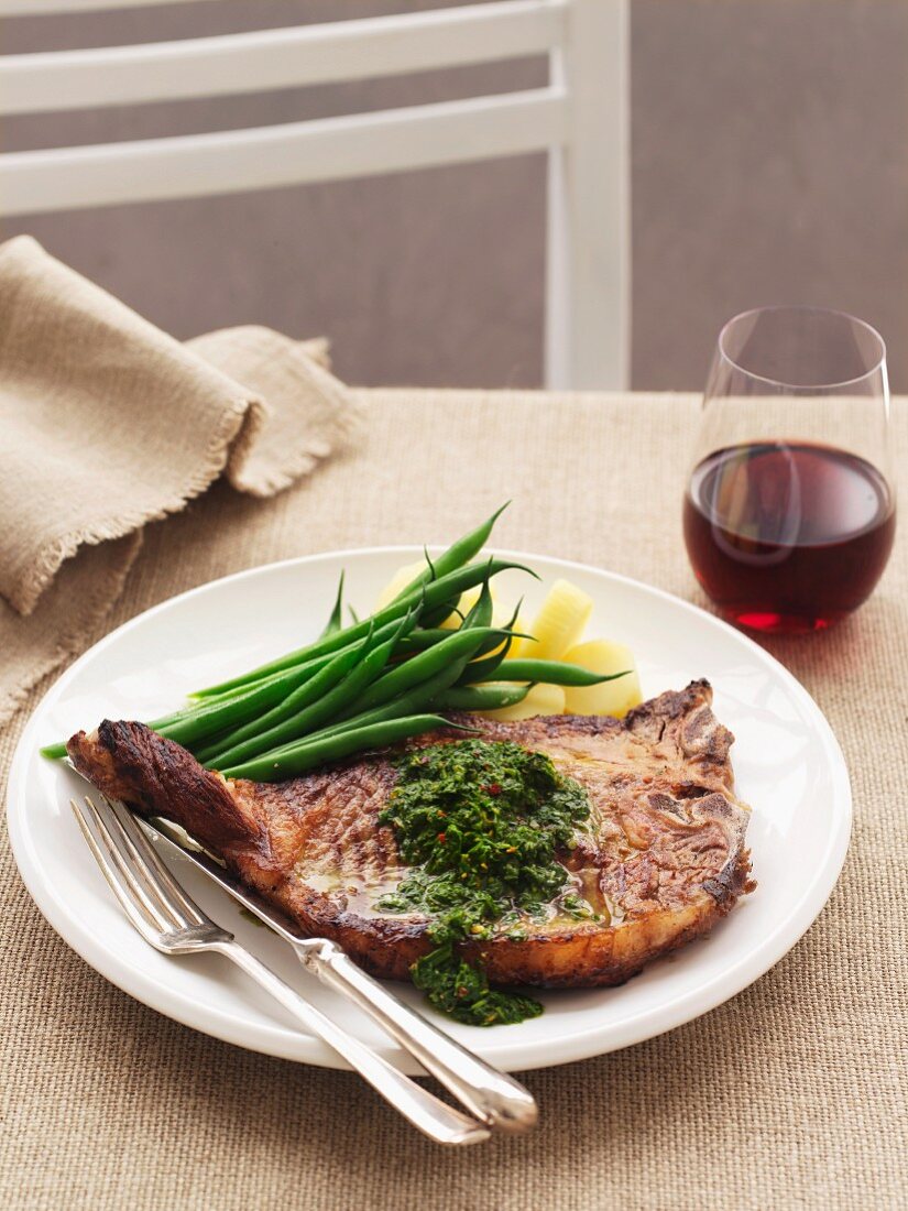 A T-bone steak with chimichurri and green beans