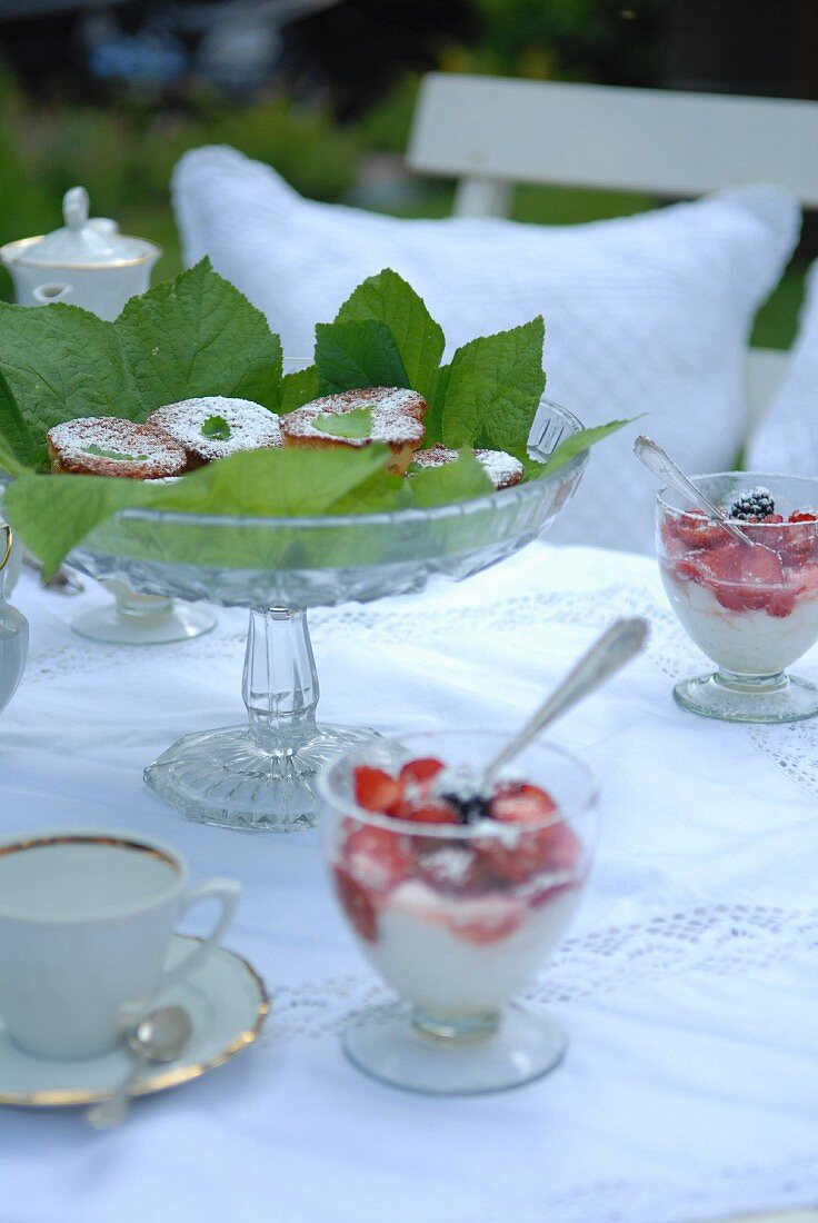 Dessertschalen mit Sahne-Beeren-Dessert; dazwischen eine mit grünen Blättern dekorierte Glasschale mit Gebäck