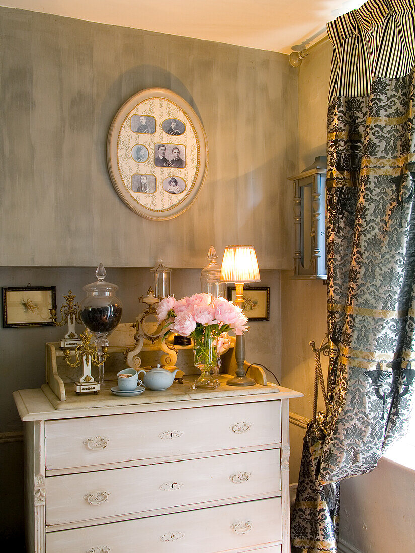 Antique chest of drawers with bouquet of flowers, patterned curtains