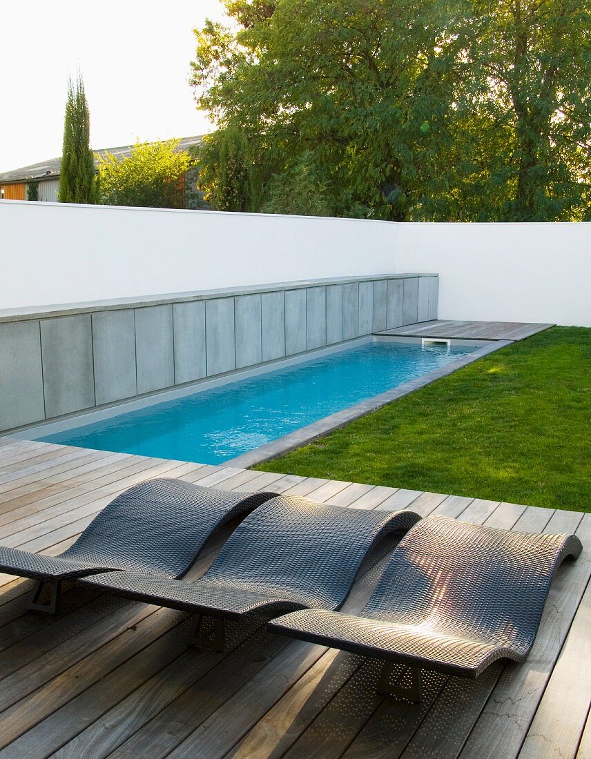 Pool and wooden deck with loungers in garden