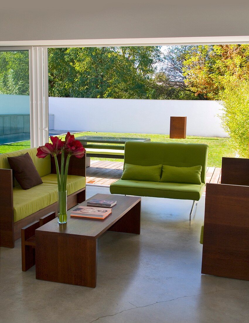 Sofa mit lindgrünen Polstern und Holzrahmengestell mit passendem Couchtisch vor raumhohem Terrassenfenster in zeitgenössischer Architektur