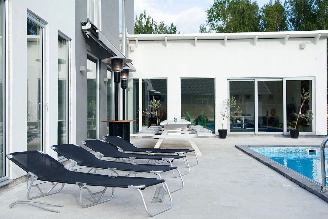 Black aluminium loungers on a concrete terrace by a swimming pool