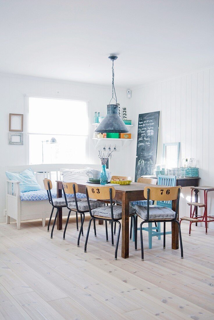 Table and old chairs from a former school and bench with cushions in dining room with white wooden floor