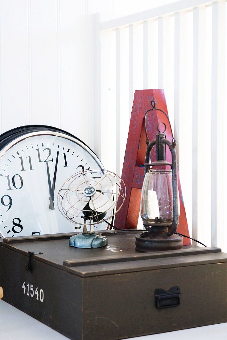 Holzkästchen mit Vintage Ventilator und Öllampe, sowie Buchstabe und Wanduhr auf weisser Ablage