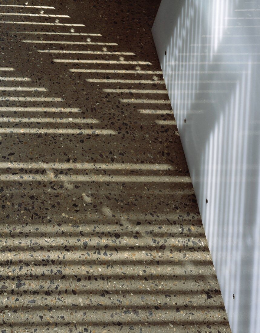 Light falling on grey composite stone floor with inclusions and white wall